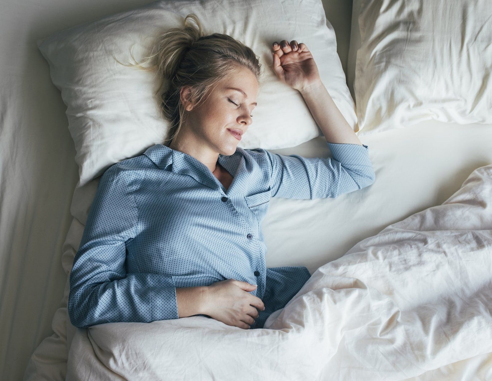 Donna che dorme fra le lenzuola indossando un pigiama azzurro
